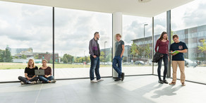 Studierende im Gespräch vor einem großen Fenster.